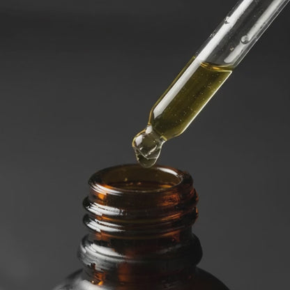 Glass pipette dispensing beard oil above an open bottle neck
